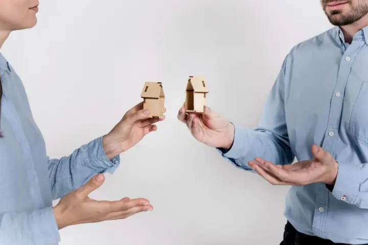 Dwie osoby trzymają miniaturowe domki, symbolizujące zniesienie współwłasności gdy współwłaściciel nie żyje.