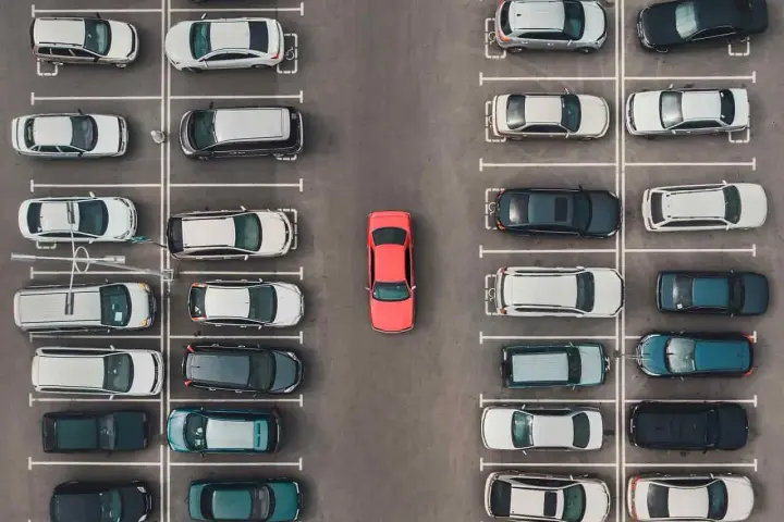 Widok z góry na parking, gdzie samochody są zaparkowane w strefie zamieszkania. W centrum wyróżnia się czerwony samochód.