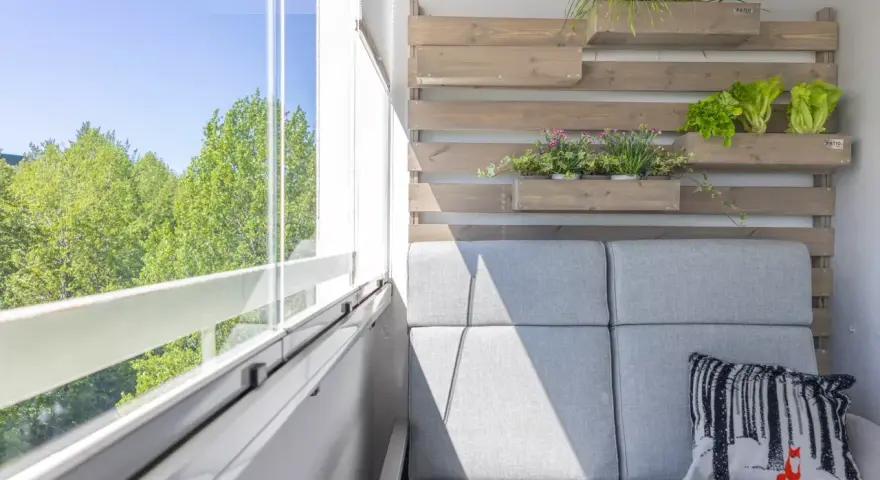 Przytulny balkon z szarą sofą, poduszką z liskiem i zielenią. Idealne miejsce, by zastanowić się, co na balkon posadzić.