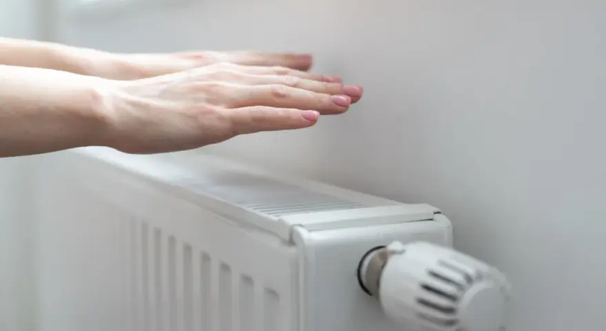 Dłonie ogrzewają się nad grzejnikiem, kiedy grzeją w blokach. Ciepło rozchodzi się po pokoju.