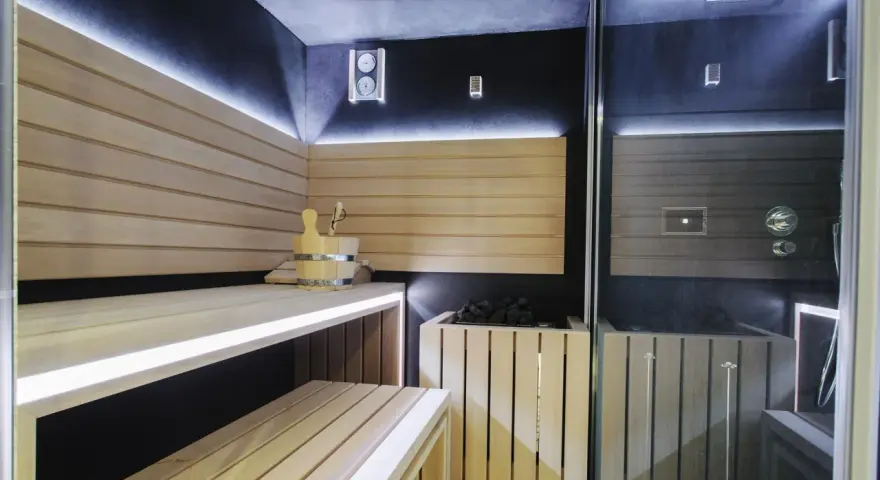 Nowoczesna sauna w domu z drewnianymi ławami, kamiennym piecem i dyskretnym oświetleniem LED. Idealne miejsce na relaks.