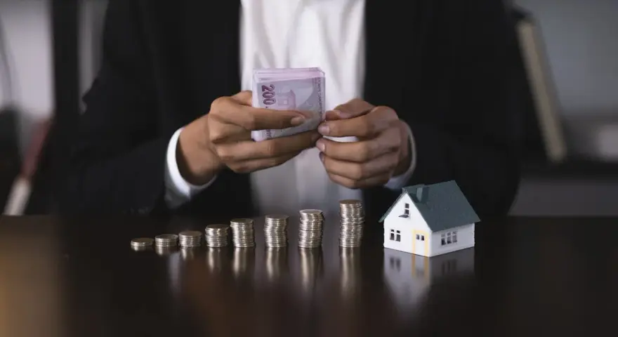 Osoba w garniturze liczy pieniądze obok modelu domu i stosów monet. Czy zaliczka jest zwrotna?