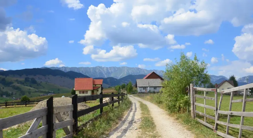 Droga wiejska z drewnianym płotem, domami i górami w tle. Współwłaściciel drogi nie wyraża zgody na jej dalsze użytkowanie.