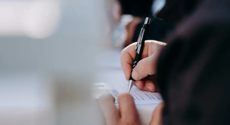Dłoń pisze długopisem na dokumencie. Kto może zameldować osobę w domu? Właściwa osoba wypełnia formularz.