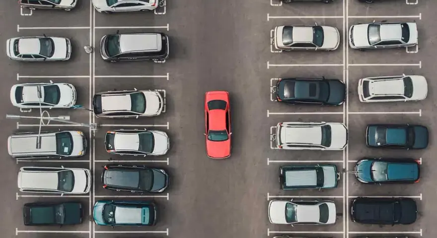 Widok z góry na parking, gdzie samochody są zaparkowane w strefie zamieszkania. W centrum wyróżnia się czerwony samochód.