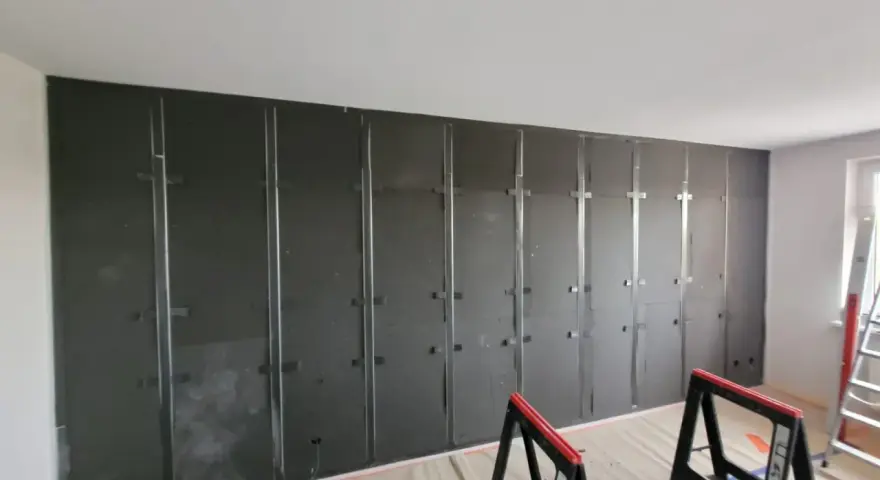 Montaż paneli wygłuszających ścianę od sąsiada. Metalowy stelaż i ciemne płyty tworzą barierę akustyczną.