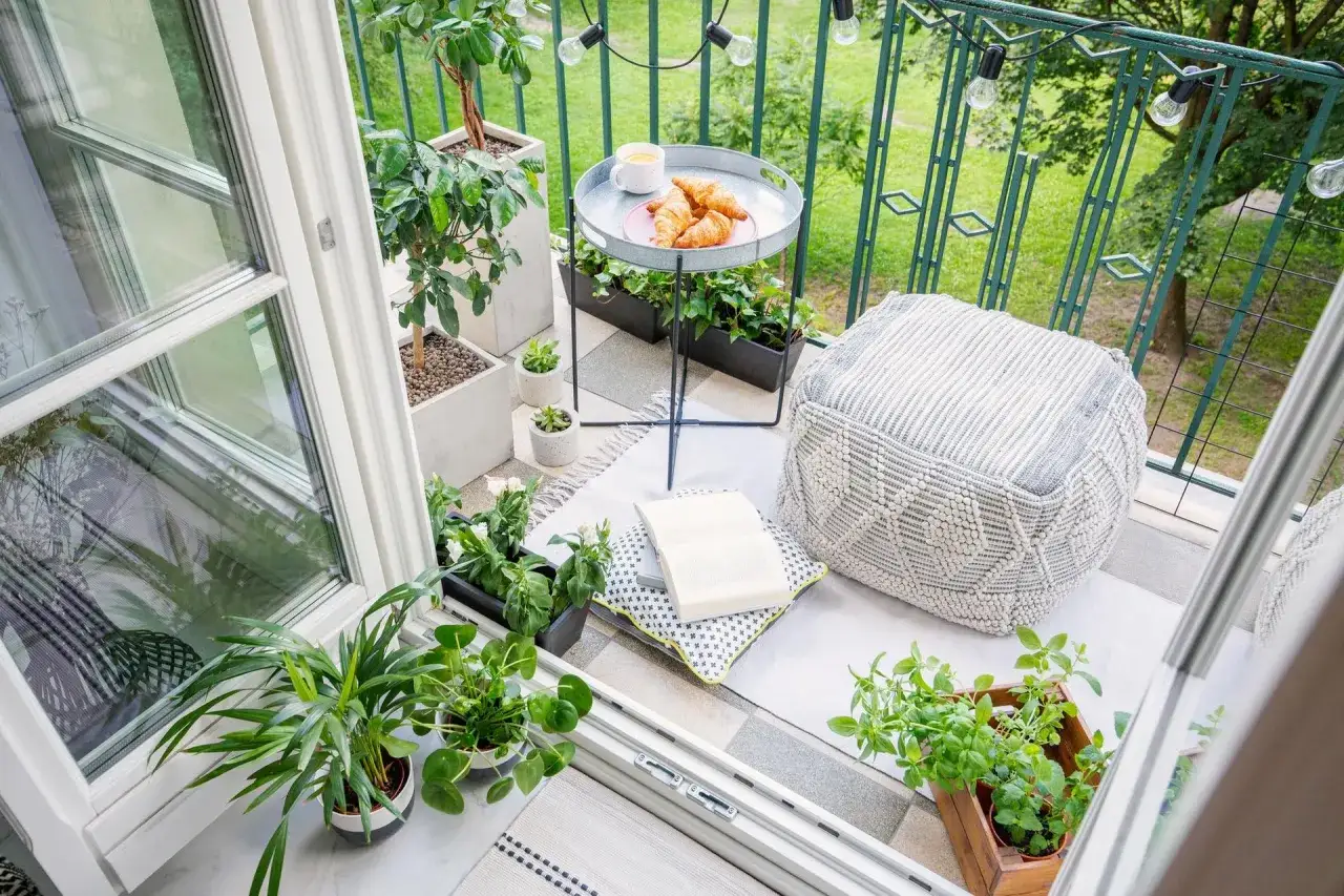 Przytulny balkon z roślinami, stolikiem z kawą i croissantami, pufą i książką. Idealne miejsce, by zastanowić się, co na balkon.