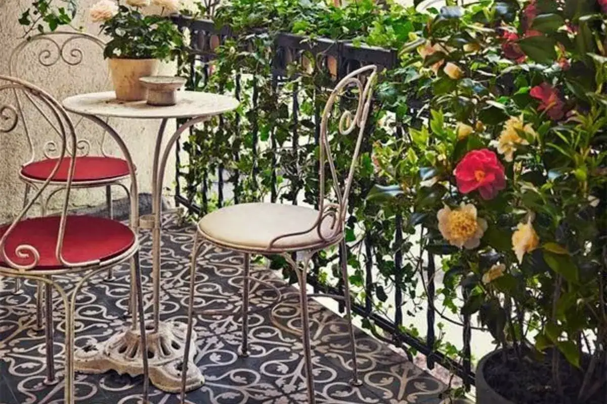 Uroczy balkon w stylu włoskim z metalowymi meblami i kwitnącymi krzewami. Idealne miejsce na poranną kawę.