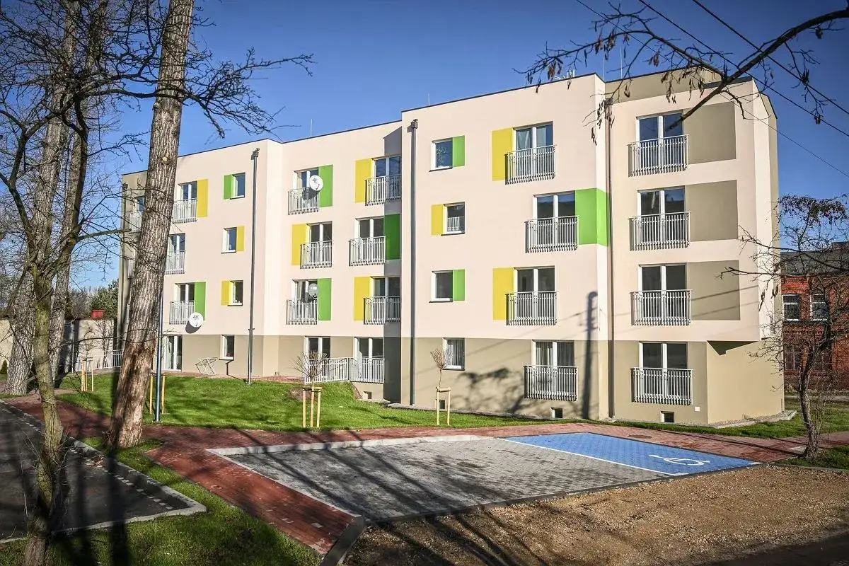 Nowy blok mieszkalny z kolorowymi akcentami. Obok parking, w tym miejsce dla niepełnosprawnych. Główny najemca mieszkania komunalnego nie mieszka, ale budynek czeka na lokatorów.