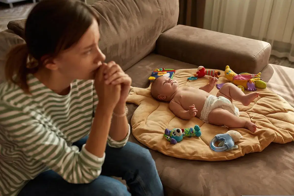 Samotna matka zamyślona nad dzieckiem na macie. Marzy o własnym mieszkaniu.