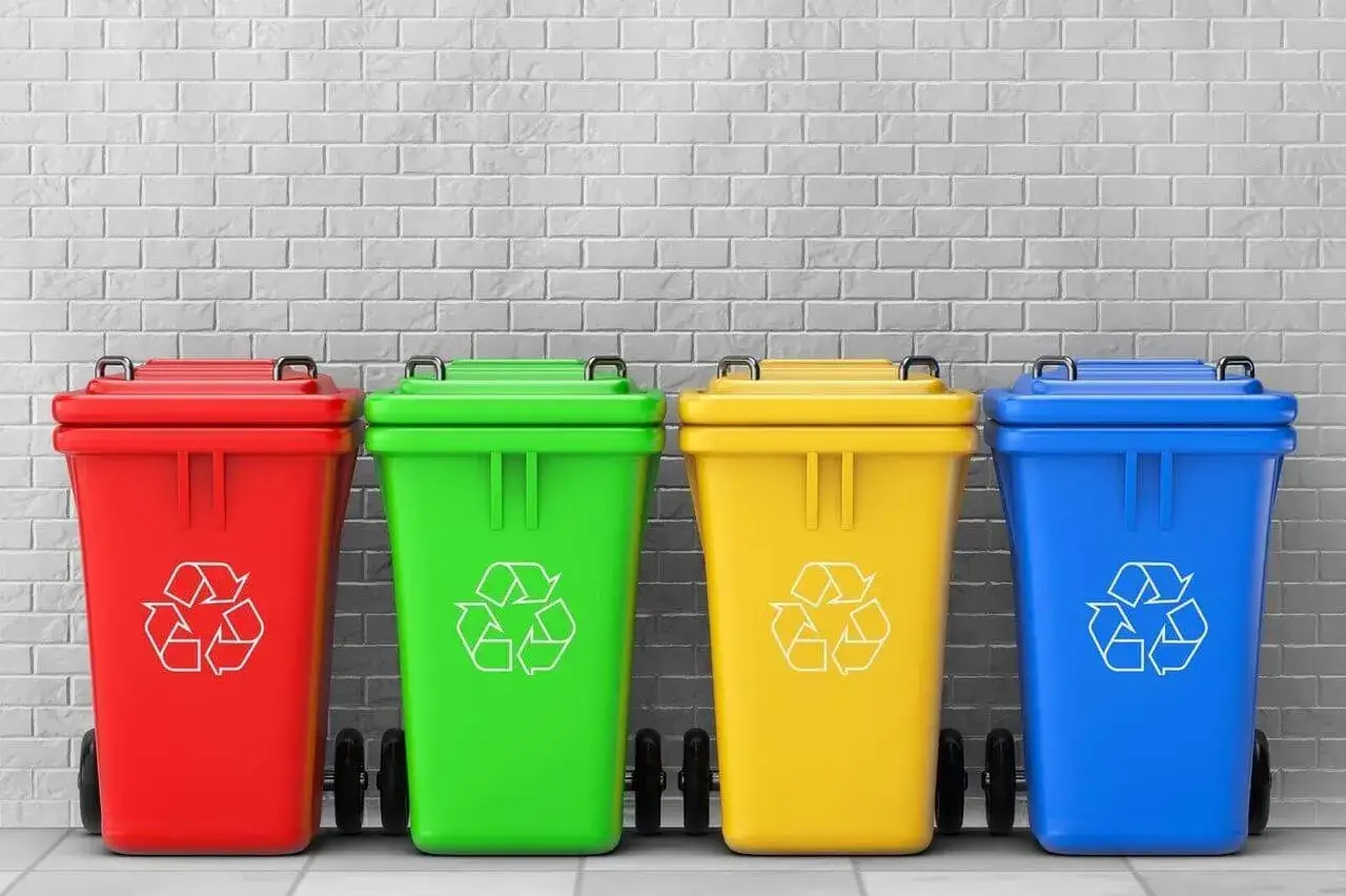 Cztery kolorowe kosze (czerwony, zielony, żółty, niebieski) z symbolem recyklingu, gotowe do segregacji śmieci.
