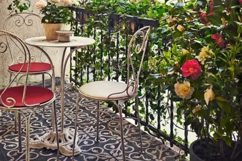 Uroczy balkon w stylu włoskim z metalowymi meblami, kwitnącymi kameliami i bluszczem. Idealne miejsce na poranną kawę.